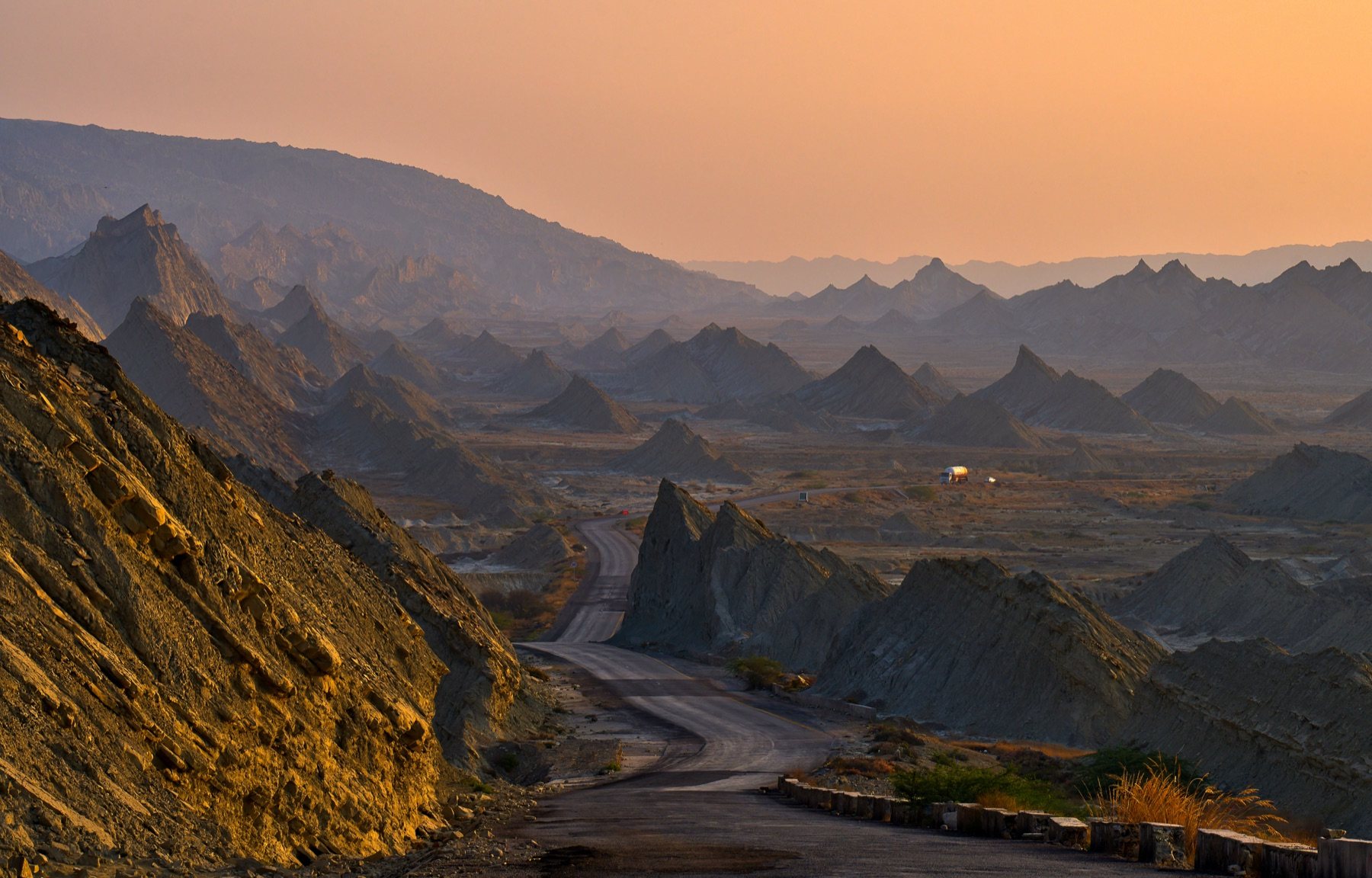 The empty Makran Coastal Highway curving through the Hingol badlands at golden hour
