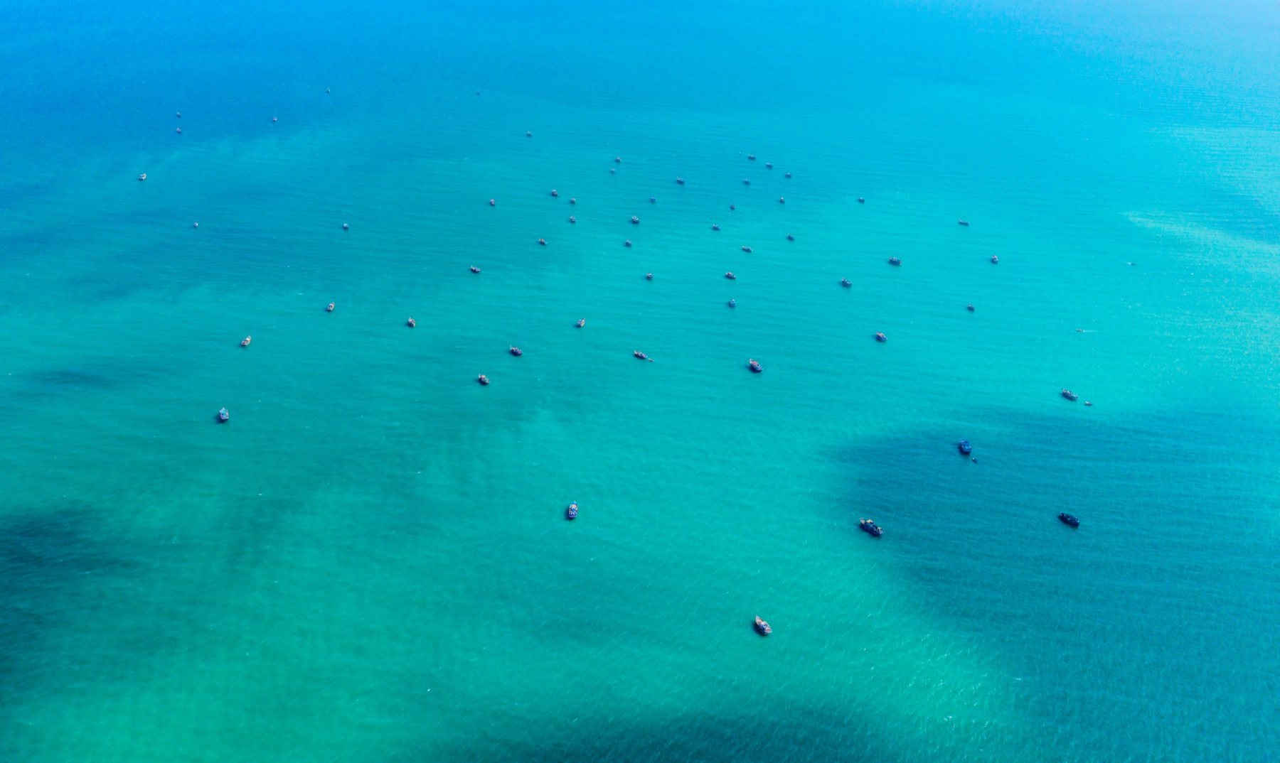 Aerial of the Pishukan fishing fleet at rest in water so clear each boat casts a shadow on the seabed