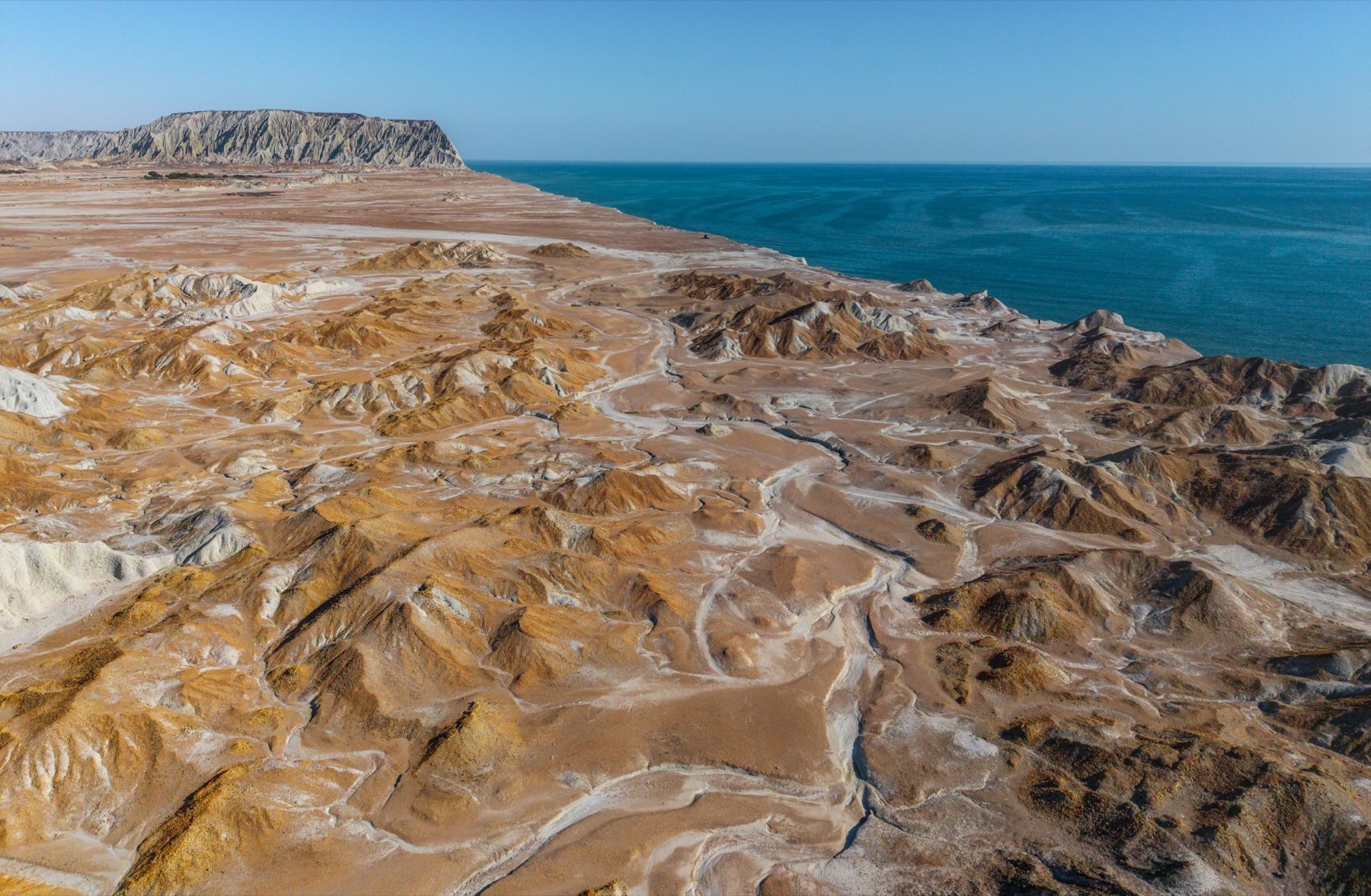 Ganz Beach — orange and white eroded badlands running into the deep blue Arabian Sea